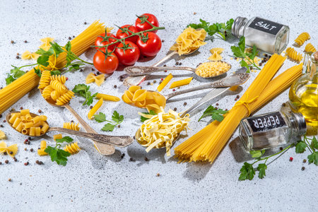 Various dried  spaghetti, noodles, pasta  set in spoons on white table background. Different shapes types raw italian pasta with herbs, olive oil, tomatoes, spices for cooking top view copy spaceの写真素材
