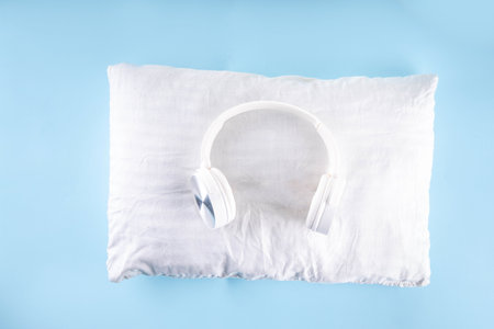 Sonic Hues and Noise for sleep concept with comfortable headphones and white pillow on light blue background top view copy spaceの写真素材