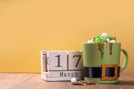 Alternative drink children's party St. Patrick's Ireland holiday. Creative decorated green mug with buckle, hot chocolate with marshmallow and green sugar sprinkles, with traditional decor of Patrick's Dayの写真素材