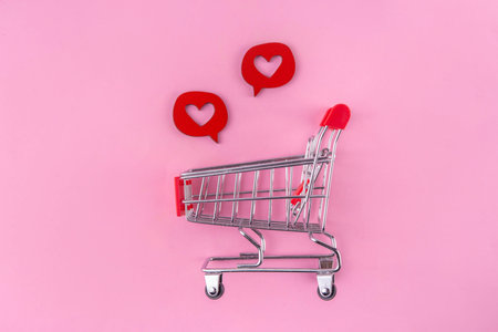 Shopping cart with heart shaped gift box pink and white background, copy space. Valentine day gifts...