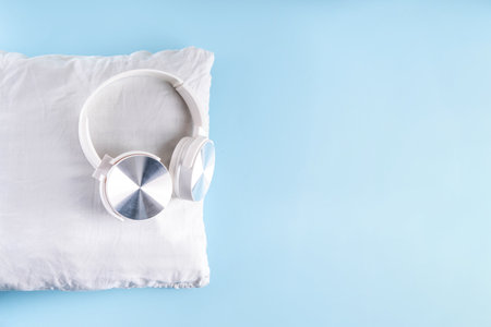 Sonic Hues and Noise for sleep concept with comfortable headphones and white pillow on light blue background top view copy spaceの写真素材