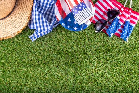 July 4, Independence Day traditional American picnic background. Plates, glasses, USA flags on green lawn or meadow grass, with blanket or tablecloth for picnic, sunglasses, copy space top viewの写真素材