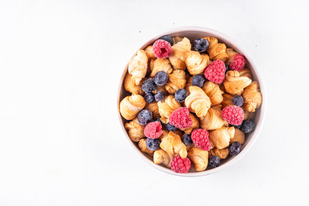 Tiny breakfast croissants cereals with fresh berries and milk. Bowl portions with trendy fresh baked...