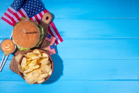 Tasty cheeseburger, chips and sauce with patriotic american flag. July 4th, Independence day picnic party food, usa themed  bbq hamburger copy spaceの写真素材