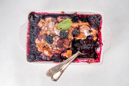 Sweet homemade mulberry cobbler pie, Sweet summer berry cobbler cake in enamel baking dish and plate, on white kitchen table copy spaceの写真素材