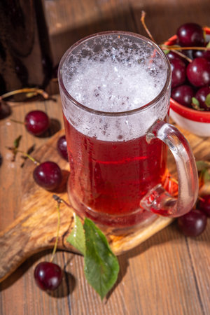 Craft cherry beer or cider alcohol drink mug and bottle on wooden table with fresh ripe cherries, copy spaceの写真素材