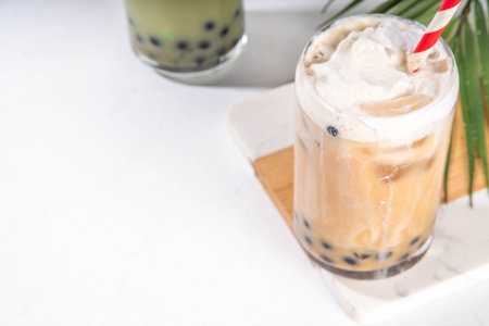 Classic and green matcha boba bubble tea with tapioca pearls and whipped non-dairy creamer on top of glass, summer cold sweet dessert drink on white table background copy spaceの写真素材