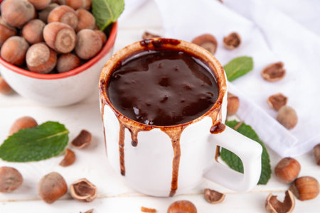Homemade Hazelnut hot chocolate in a white mug, with a lot of hazelnuts on white wooden background, copy spaceの写真素材