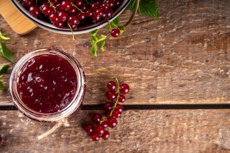 Organic red currant berry jam or marmalade in small jar with fresh berries on wooden table, copy...