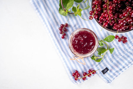 Organic red currant berry jam or marmalade in small jar with fresh berries on kitchen table, copy...