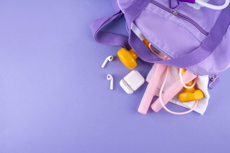 Sport and fitness background. Women's sports bag with dumbbells, bottle of water, towel, jump rope, headphones, accessories for sports and fitness on light purple background, copy spaceの写真素材