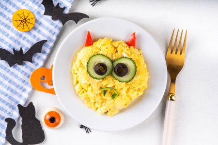 Halloween breakfast scrambled eggs shaped and decorated like cute monster, with fresh vegetables, funny kids Halloween food simple recipe ideaの写真素材