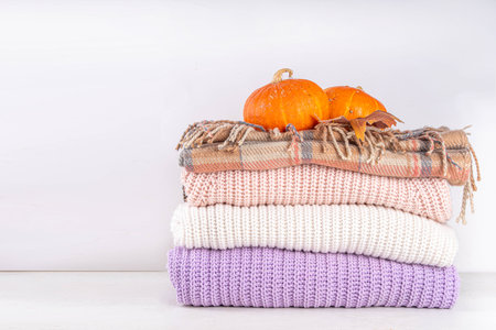 Stack of autumn knitted wool clothes, warm sweaters, with fall leaves in female hands on white background. Autumn sale promotions, clothes cleaning, announcements mock-up background copy spaceの写真素材