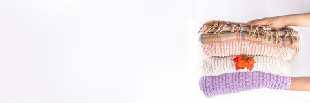 Stack of autumn knitted wool clothes, warm sweaters, with fall leaves in female hands on white background. Autumn sale promotions, clothes cleaning, announcements mock-up background copy spaceの写真素材