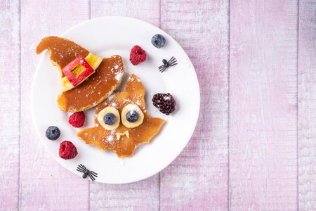 Halloween kids food treat. Funny pancakes in form of cute bat with witch hat. Breakfast snack for child's Halloween party, with berries & candyの写真素材