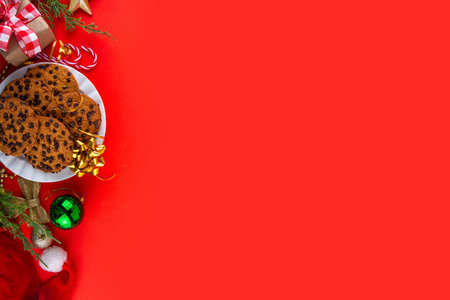 Christmas festive background with tasty hot chocolate, crispy chocolate drops cookies, Christmas decor, baubles, santa hat and gift boxes, high-colored bright red green background copy spaceの写真素材