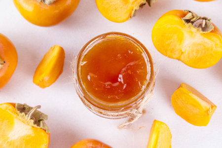 Persimmon jam. Sweet autumn homemade jam or marmalade canning preserves in a jar, with whole and cut persimmon c in the backgroundの写真素材