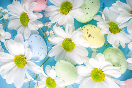 Happy easter greeting, invitation card background. Spring flowers composition with colorful easter eggs and spring flowers on blue wooden table, with copy space for text. Flat lay, top view.の写真素材