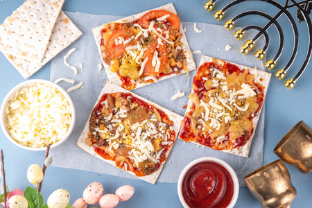 Matzah Pizza on light blue background with ingredients, cheese, tomato sauce. Food ideas and recipe...