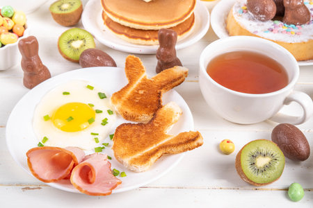 Easter holiday sweet breakfast, brunch. Easter decorated belgian waffles, pancakes, breakfast cereals and milk, fried eggs with toasts and bacon, Easter chocolate eggs and bunny, with spring flowersの写真素材
