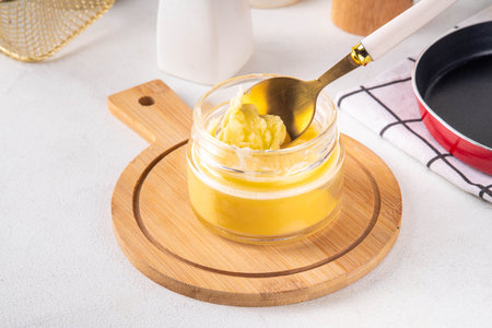Homemade ghee butter in small glass jar on white kitchen table background, copy space. Melted...