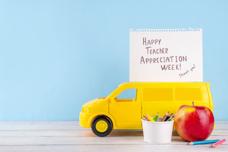 Teacher Appreciation Week background with school supplies and traditional gifts, bouquet of spring flowers with pens, pencils, notebooks, notepads, school bus toy, greeting card to teacher from childの写真素材