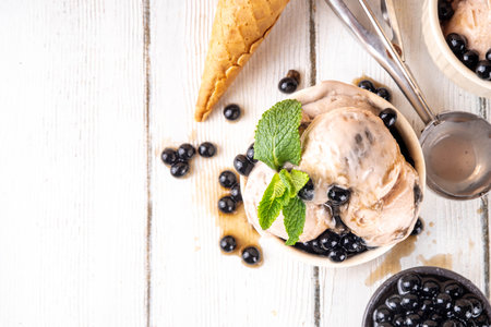 Bubble milk tea ice cream, sweet taiwanese asian style milky tea with Kuromitsu, black boba or tapioca pearls and syrup, in portioned bowls with ice cream cones, white wooden table copy spaceの写真素材