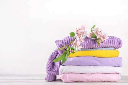 Stack of pastel colored spring clothes with blossom flowers. Spring sale concept, fashion discounts store advertising. Spring cleaning, laundry backgroundの写真素材