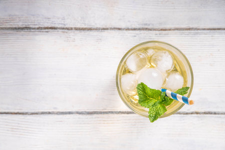 Cold vanilla cream soda drink. Tasty sweet non-alcohol beverage for hot summer days, with a lot of crushed ice and mint decor, on white wooden table copy spaceの写真素材