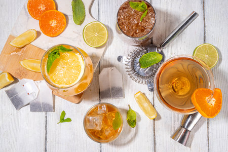 Trendy Tea Inspired cocktail set from green, oolong, black, chai and other tea blends. Sparkling tea soda, cold summer drinks with syrup, lemon, lime and mint, on sun lighted white wooden backgroundの写真素材