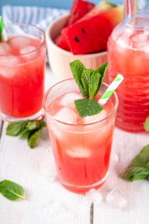 Homemade watermelon lemonade, sweet refreshing summer drink, iced watermelon juice with mint decor and striped straw, light blue and wooden background, copy spaceの写真素材