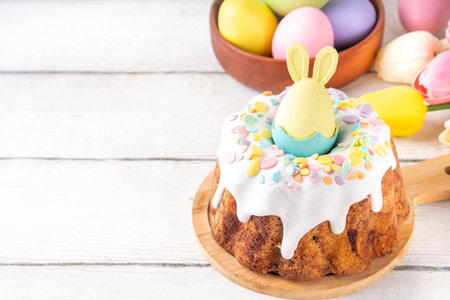 Traditional Easter cake decorated with sugar icing and sprinkles, with festive spirit decor and flower bouquet. Easter celebrations holiday table with pastel colored Easter eggs and bunny rabbitsの写真素材