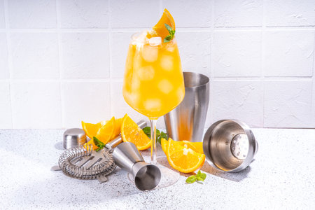 Orange and mint alcohol cocktail, aperol spritz, mimosa drink in long cocktail glass, with fresh orange slice garnish, white tiled background with bar utensils, copy spaceの写真素材