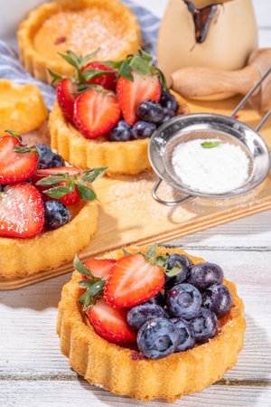 Sponge mini tart cakes with summer berry. Portioned vanilla dessert cups with fresh strawberry, blueberry, raspberry, on white wooden background copy spaceの写真素材