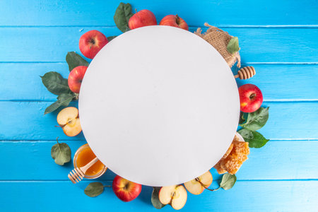 Jewish holiday Rosh Hashanah or apple feast day concept, with red apples, apple leaves, honey in jar and honeycombs light blue wooden background copy space aboveの写真素材