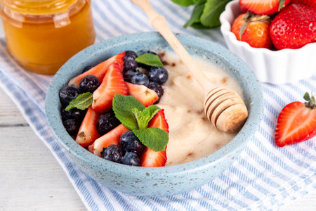 Cream of Wheat semolina porridge with fresh summer berry. Portion of breakfast whole grain creme de  semolina with dairy milk, strawberry, blueberry and honeyの写真素材