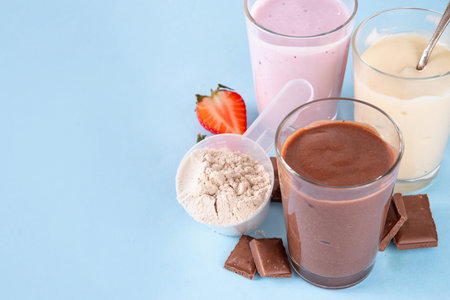Quick and simple protein pudding. Healthy summer cold dessert. Three glasses with vanilla, chocolate and berry protein pudding, with chocolate slices, fresh strawberry, blueberry, protein powder scoopの写真素材