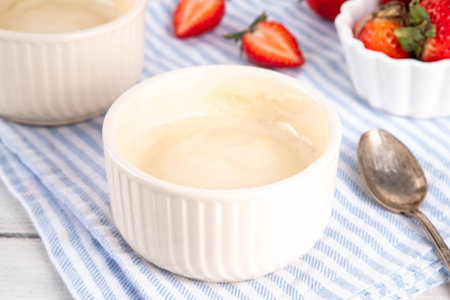 Vanilla or white chocolate pudding dessert, in ceramic portioned bowl on kitchen table, with fresh strawberriesの写真素材