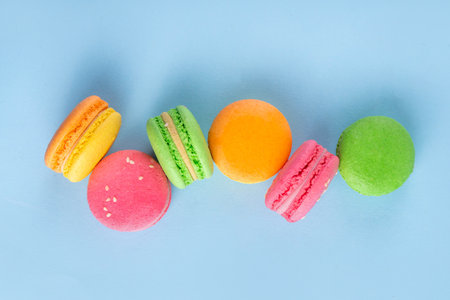 Bright and colorful sweet macaroons dessert with fresh berries. Pink, orange, yellow and pistachio green tasty macaron cookies on light blue background copy spaceの写真素材