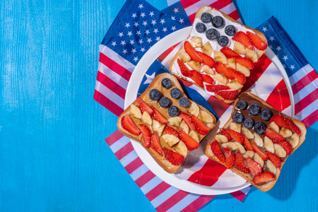 July 4 breakfast sandwiches, holiday snack or brunch with peanut butter, chocolate and cheese spread, with strawberries, blueberries and banana in the shape of america patriotic flagの写真素材