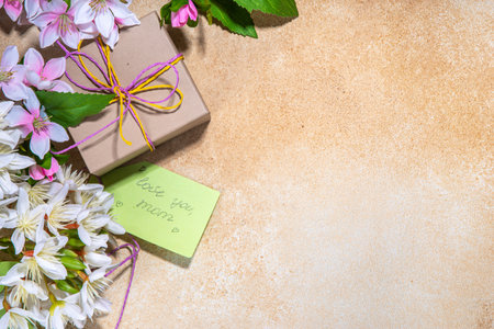 Mother day greeting card background with present and flowers. Gift box with festive ribbon, tag Love you mom, spring bloom flowering branches bouquet flatlay copy spaceの写真素材