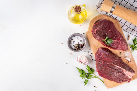 Raw meat steaks ready for cooking grilling. Two beef steaks on cutting board, with herbs, spices, olive oil, on cooking table top view copy spaceの写真素材