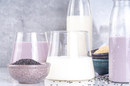Black and white sesame milk, Alternative vegan non-dairy milk drink on glass and bottles with sesame seeds on light stone background. Raw food, vegetarian natural organic food dietの写真素材