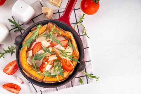Homemade breakfast savory dutch baby pancake, Portioned frying pan with savory dutch baby pancake with tomatoes, arugula and cheeseの写真素材