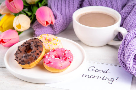 Small sugar glazed donuts with coffee latte cup, tulip flowers, sweater, tulip flower bouquet and note Good Morning. Spring holiday, Mother Day, Woman day, Birthday greeting card backgroundの写真素材