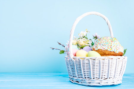 Traditional Easter basket with Easter cake, colorful pastel colored eggs, bunny rabbits decor and...
