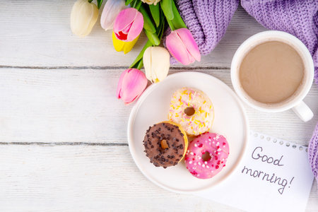 Small sugar glazed donuts with coffee latte cup, tulip flowers, sweater, tulip flower bouquet and note Good Morning. Spring holiday, Mother Day, Woman day, Birthday greeting card backgroundの写真素材