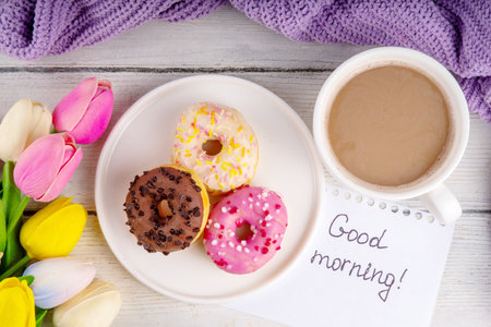 Small sugar glazed donuts with coffee latte cup, tulip flowers, sweater, tulip flower bouquet and note Good Morning. Spring holiday greeting card backgroundの写真素材