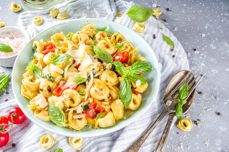 Italian ravioli, tortellini pasta with parmesan cheese and vegetables - spinach, tomatoes, mushrooms and basil, On grey stone background copy spaceの写真素材
