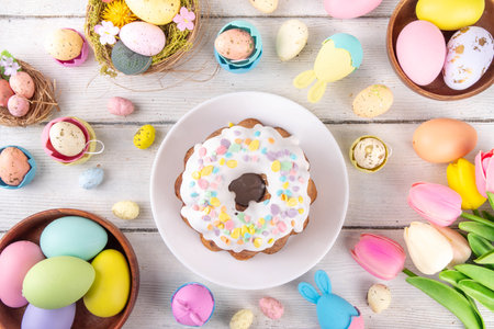 Traditional Easter cake decorated with sugar icing and sprinkles, with festive spirit decor and flower bouquet. Easter celebrations holiday table with pastel colored Easter eggs and bunny rabbitsの写真素材